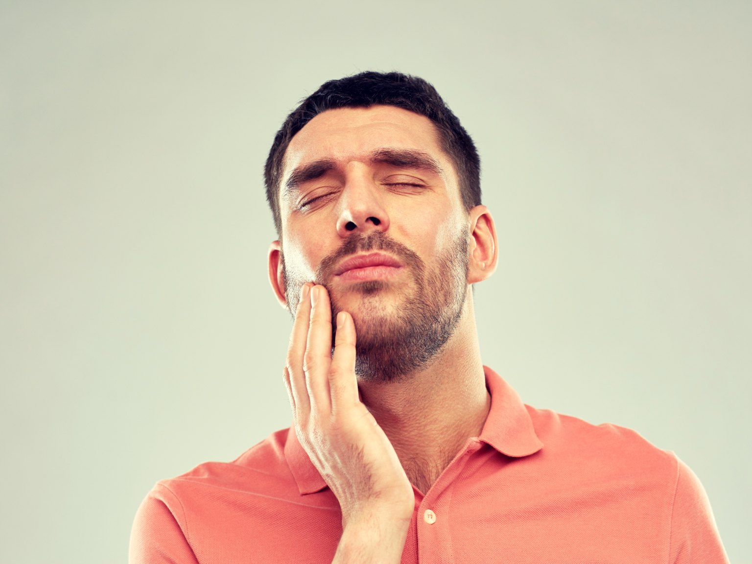 A man with his eyes shut in pain, holding his jaw