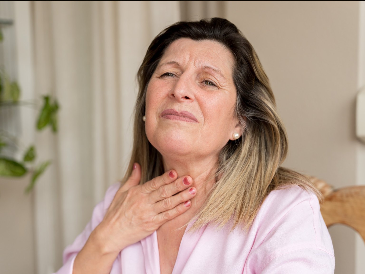 A woman holding her throat, wincing as she swallows