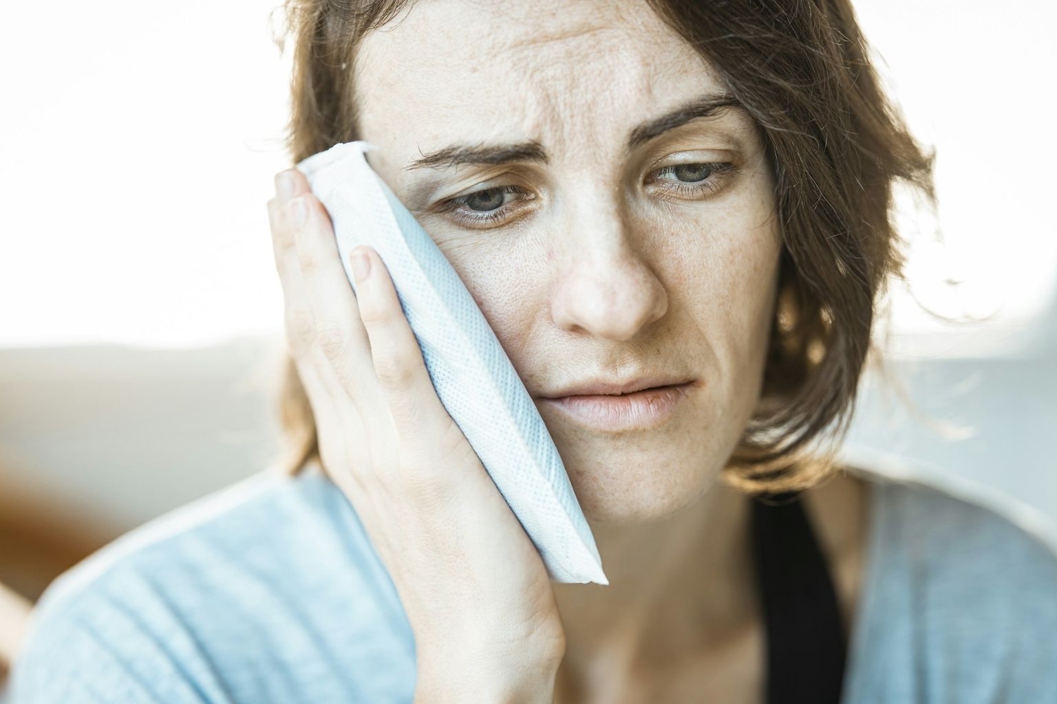 A woman holding a cold compress to her cheek