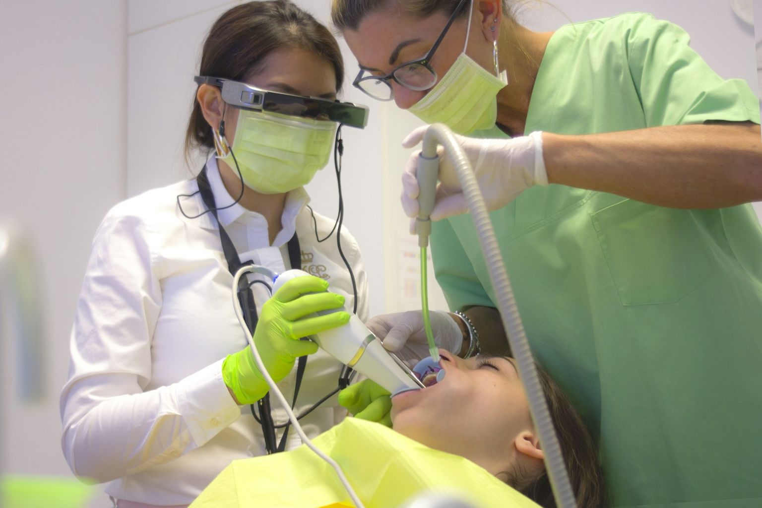 A dentist in loupes working with an assistant