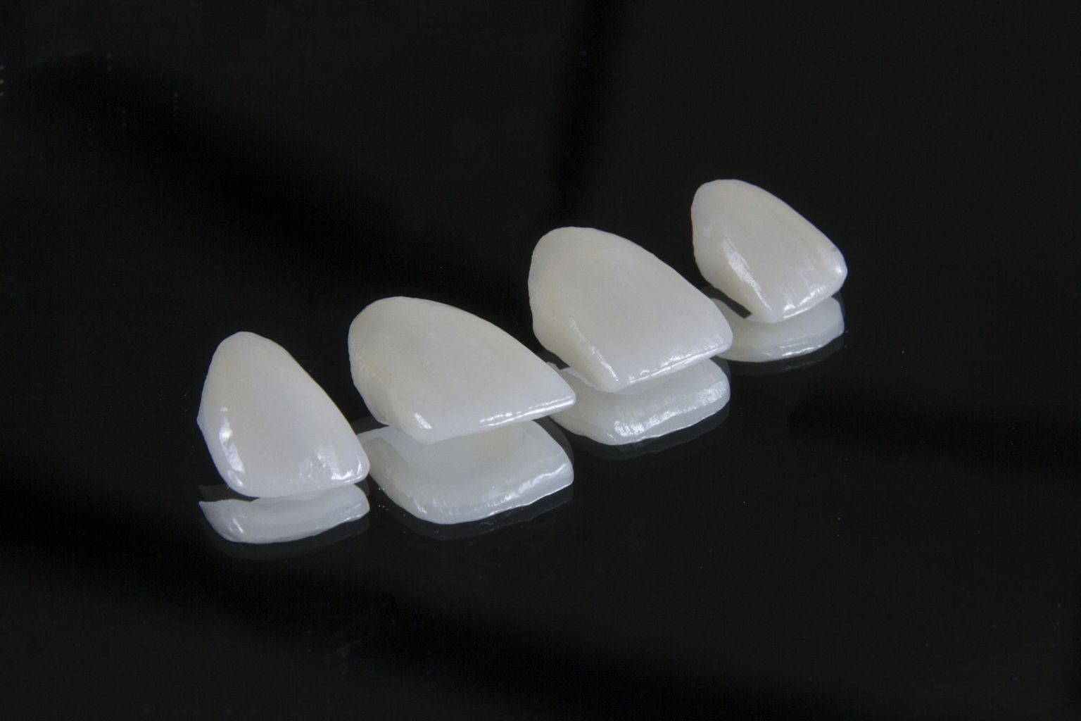 Four porcelain veneers on a black surface