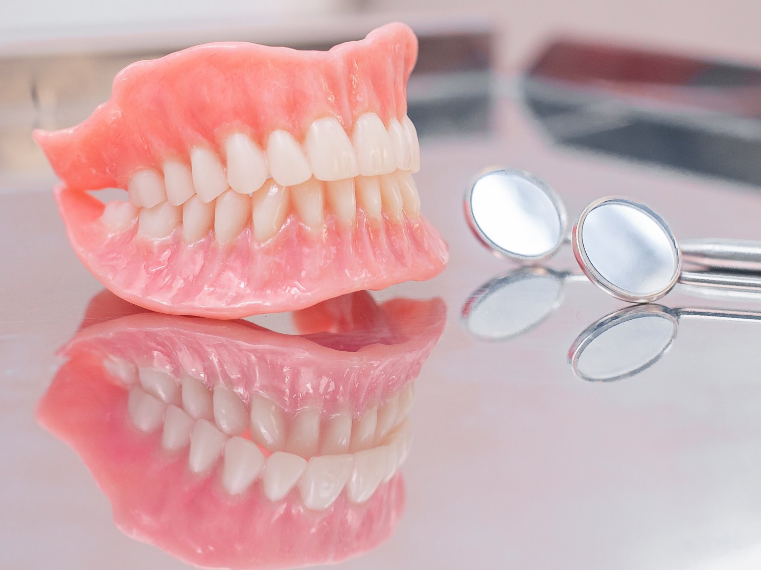 A full set of dentures on a reflective tray beside two dental mirrors