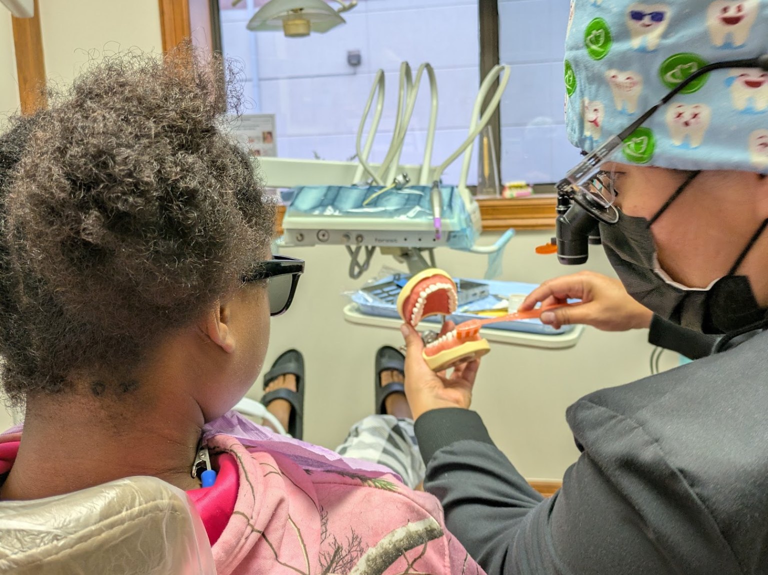 A hygienist showing a young patient how to brush on a model of the teeth