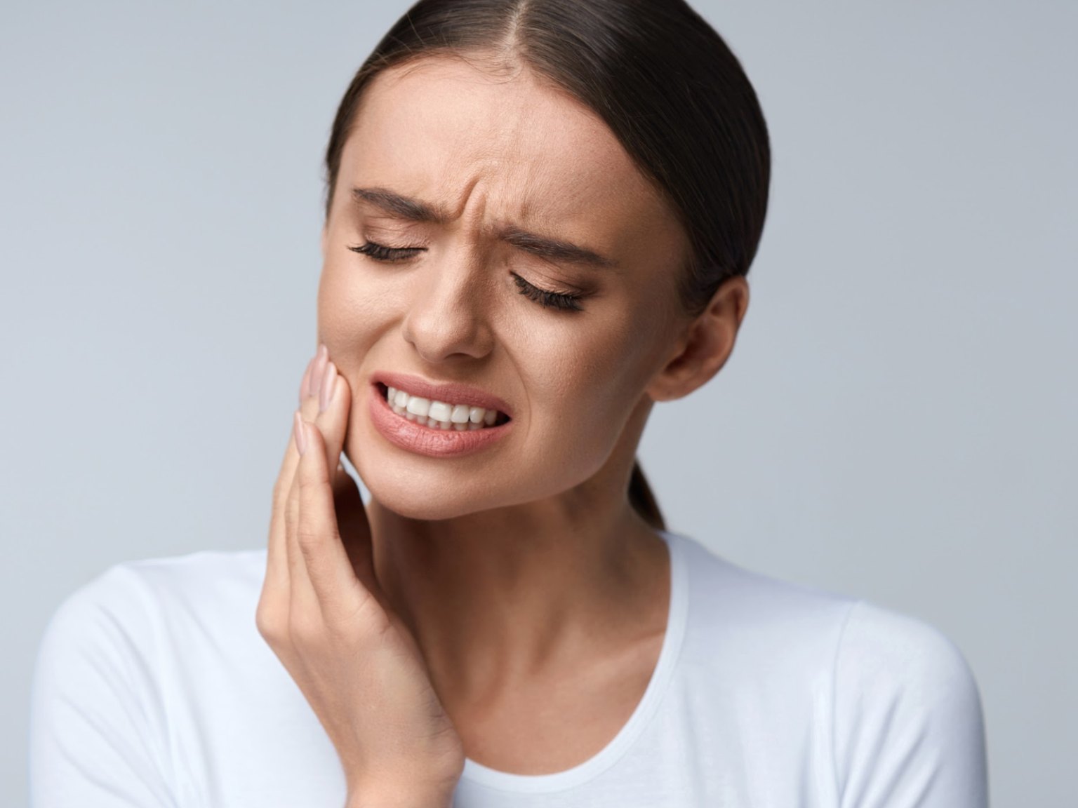 A woman wincing with her hand on her cheek from a sensitive tooth