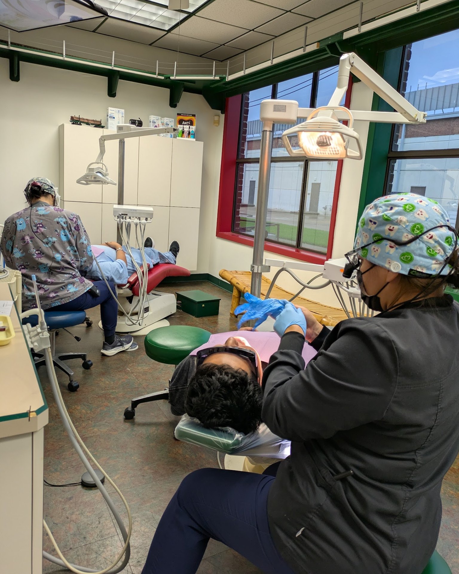 Two assistants at work in a treatment room with tall windows, a patient reclined in each chair