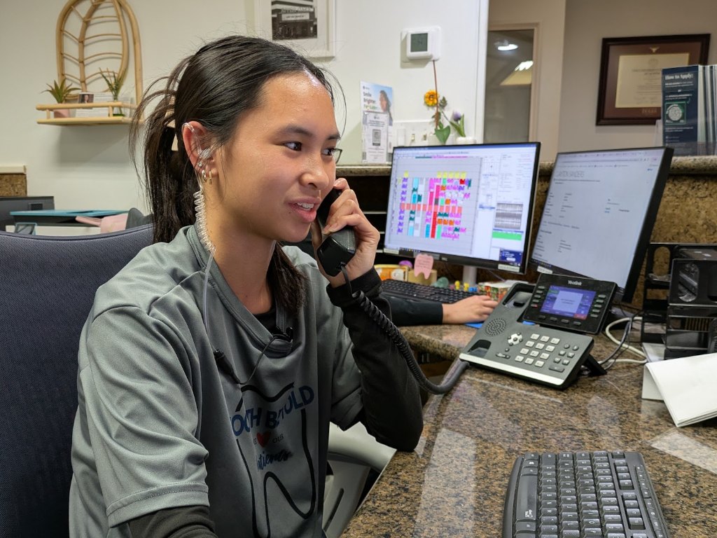 A receptionist booking a visit by phone at the front desk, the schedule open on screen