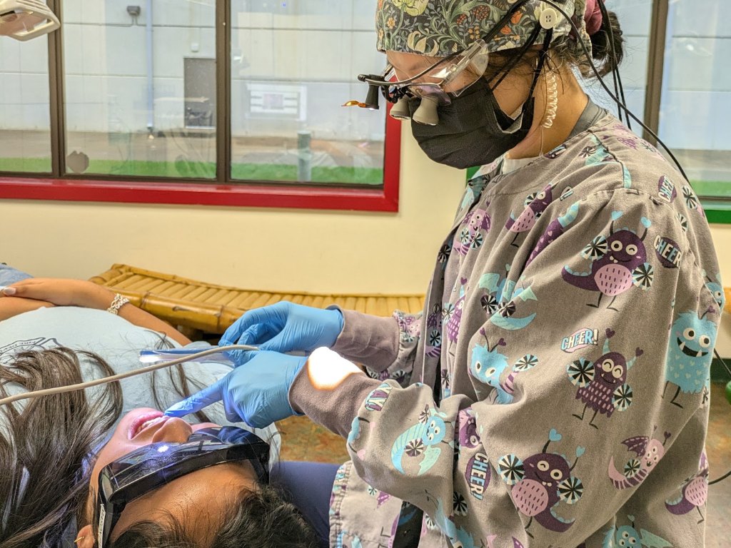 A hygienist in magnifying loupes treating a patient reclined in the chair