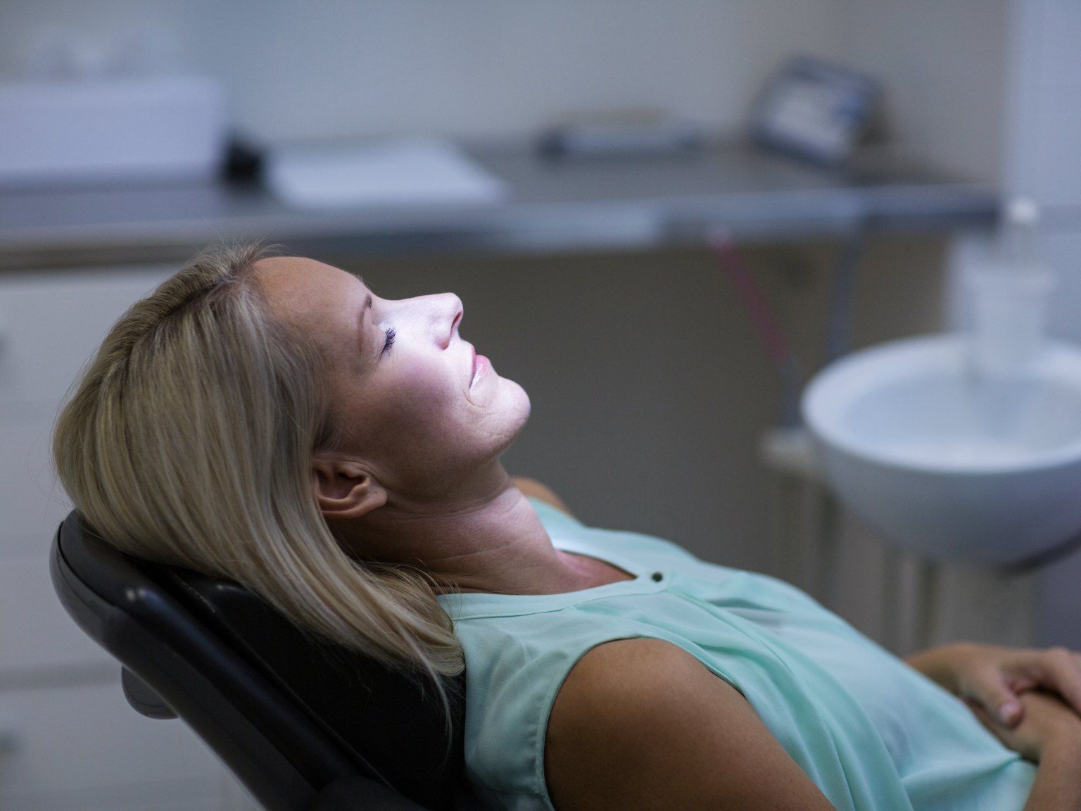 A woman lying back in a dental chair, eyes closed and hands folded, fully at ease