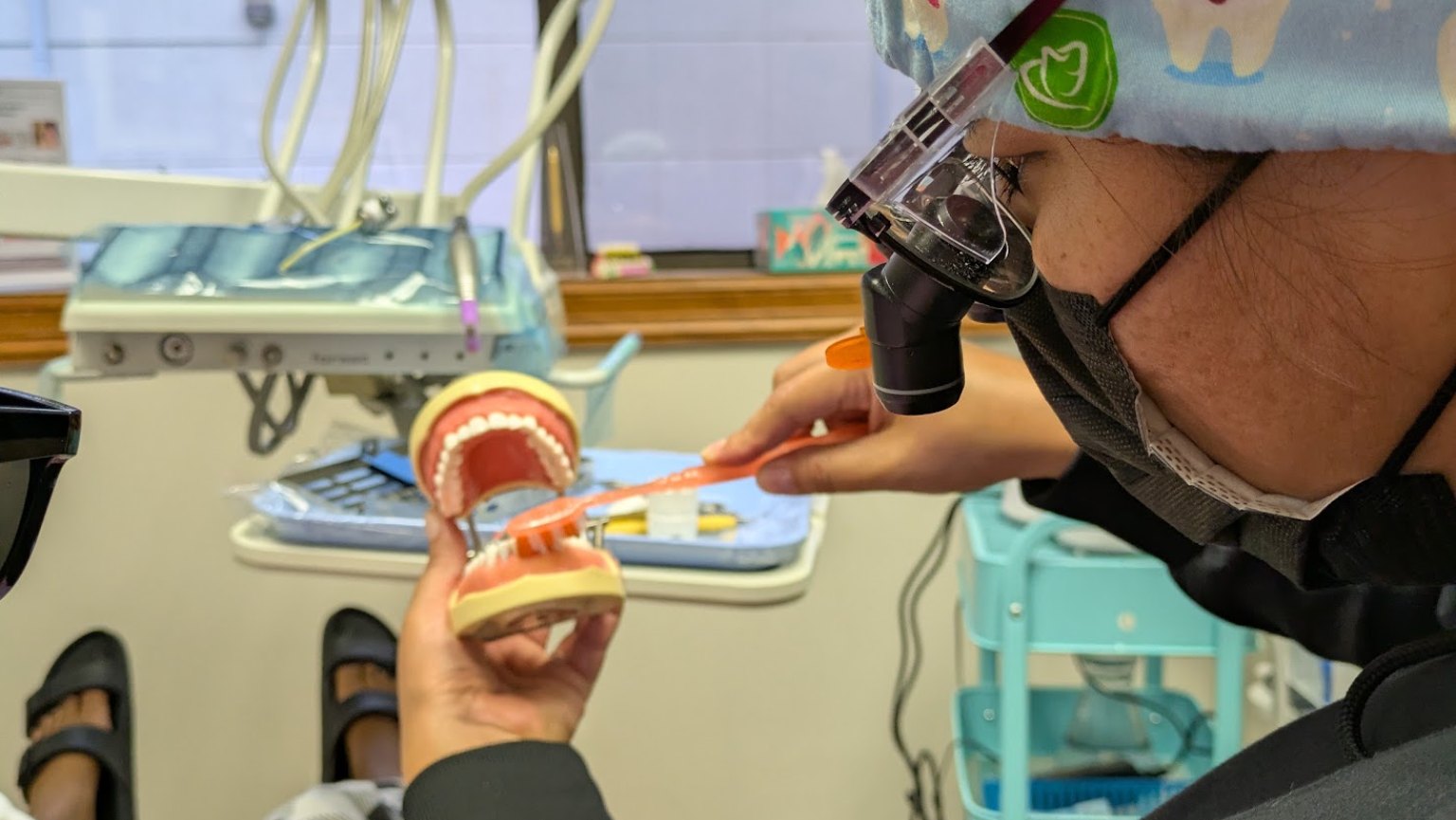 A hygienist in loupes demonstrating brushing on a model of teeth