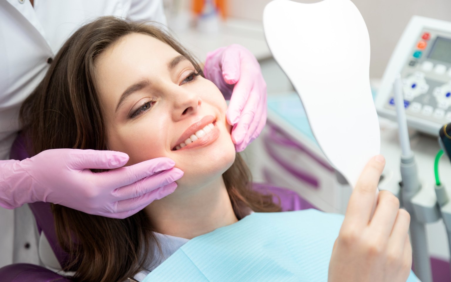 A woman in the dental chair checking her smile in a hand mirror