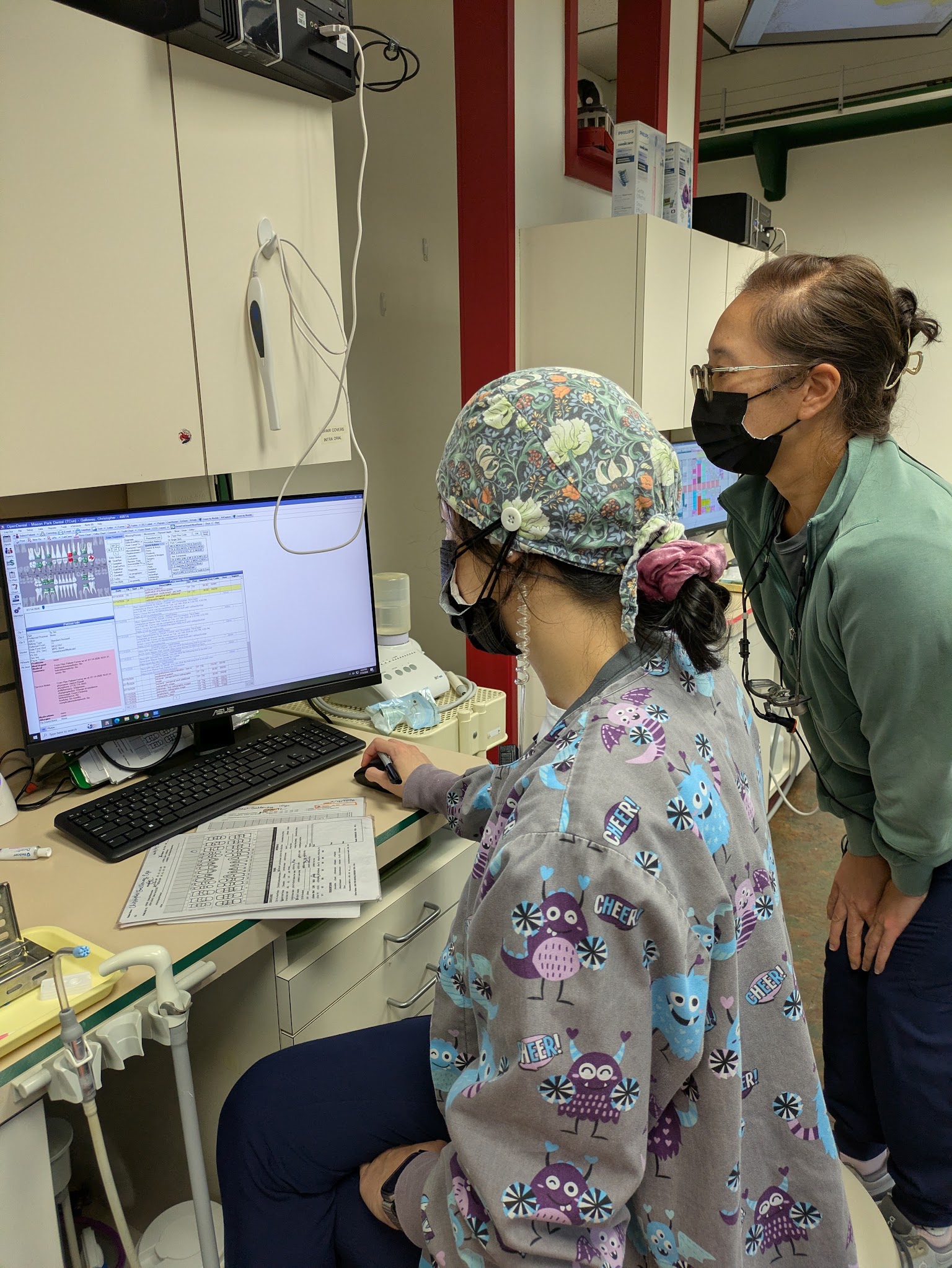 A hygienist charting at the treatment room computer with a colleague