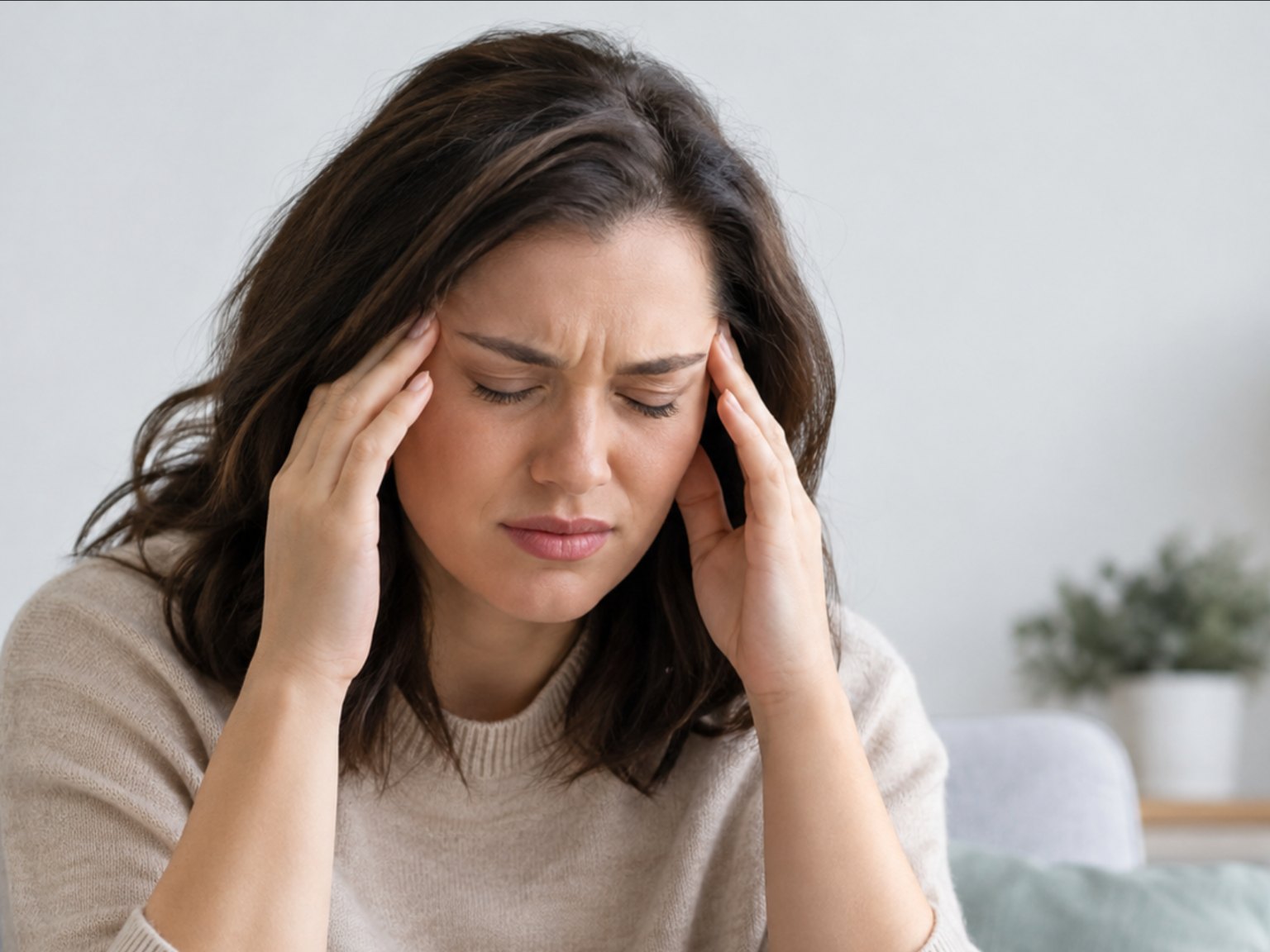 A woman on a sofa, eyes closed, pressing her temples with a headache