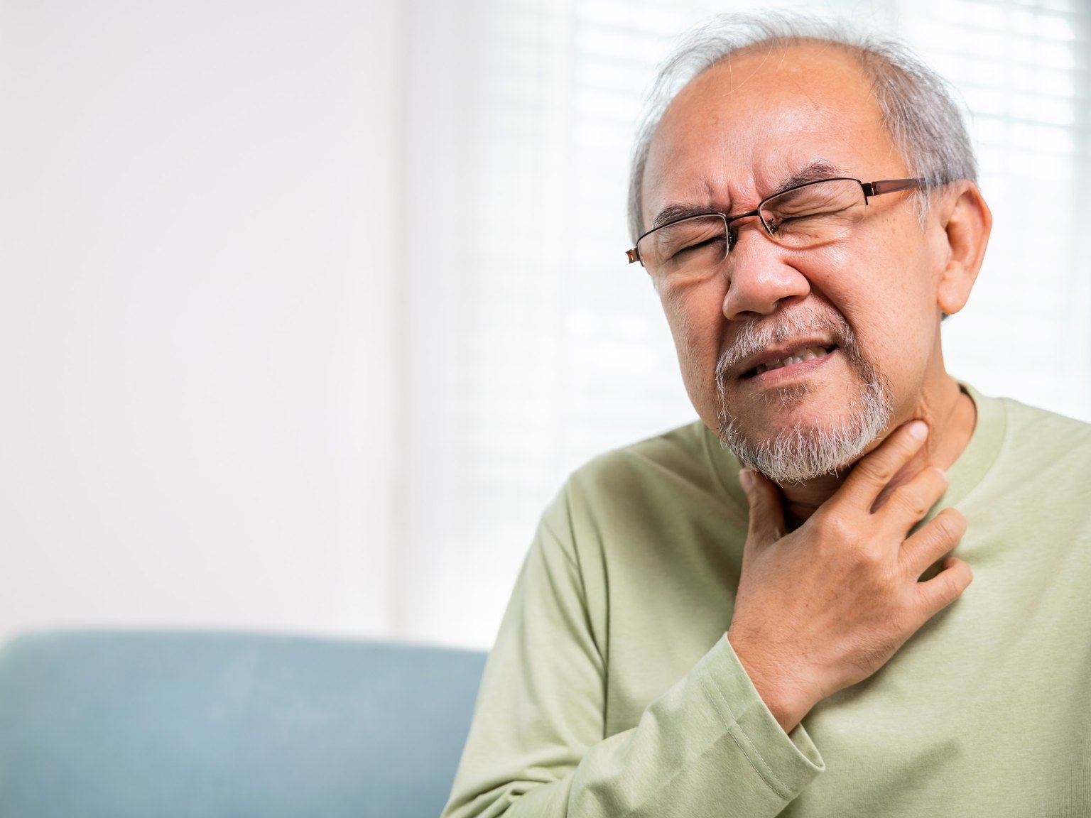 An older man in glasses gripping his throat with a pained expression