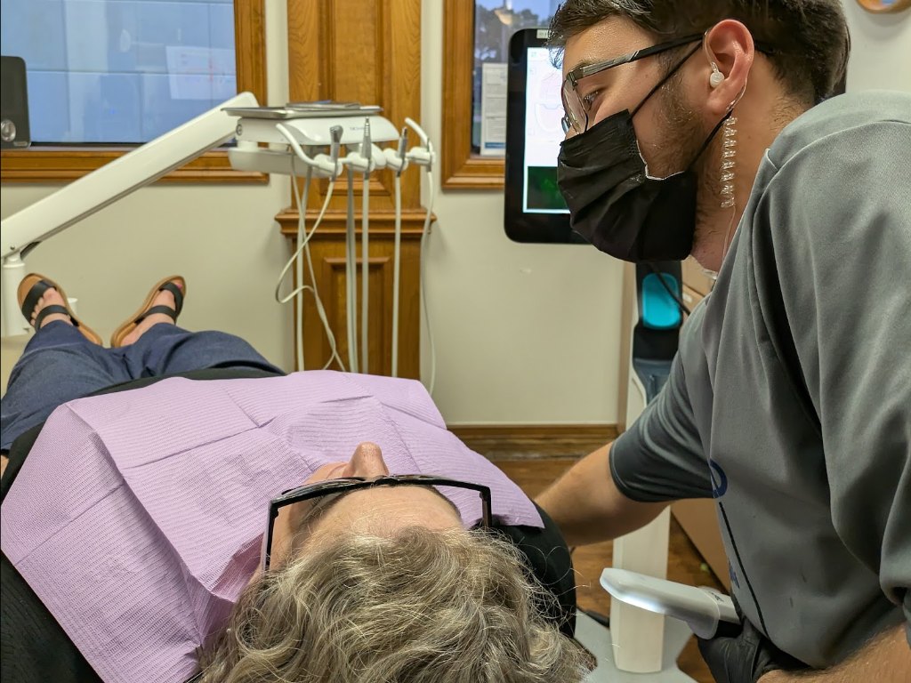 A clinician leaning over a reclined adult patient in the treatment chair
