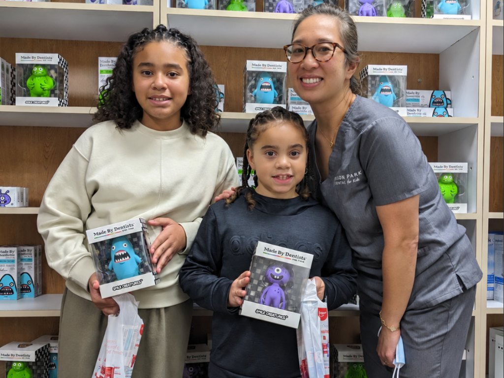 Two young patients holding toy prizes beside a smiling team member