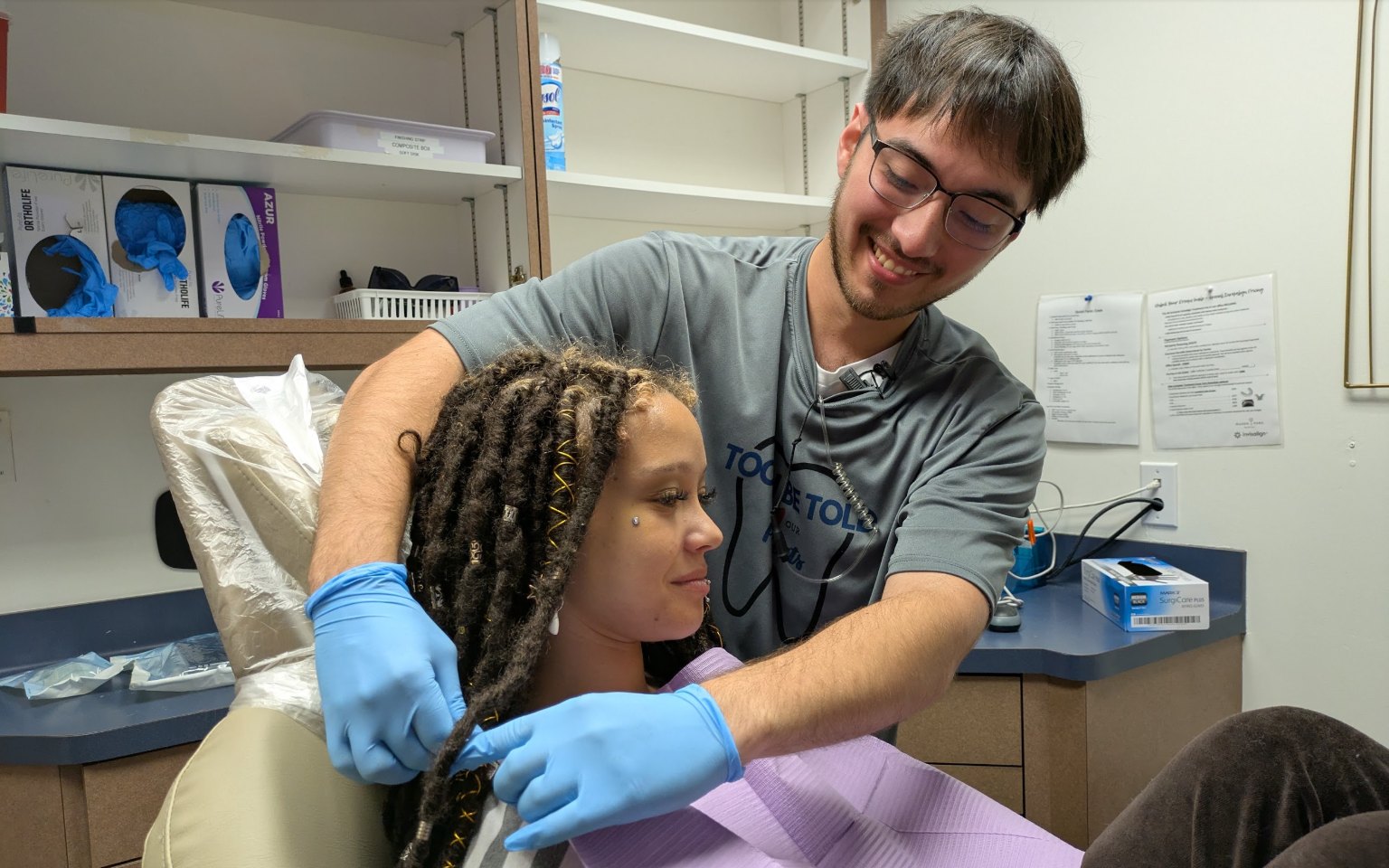 A team member fastening a bib on a smiling patient in the chair
