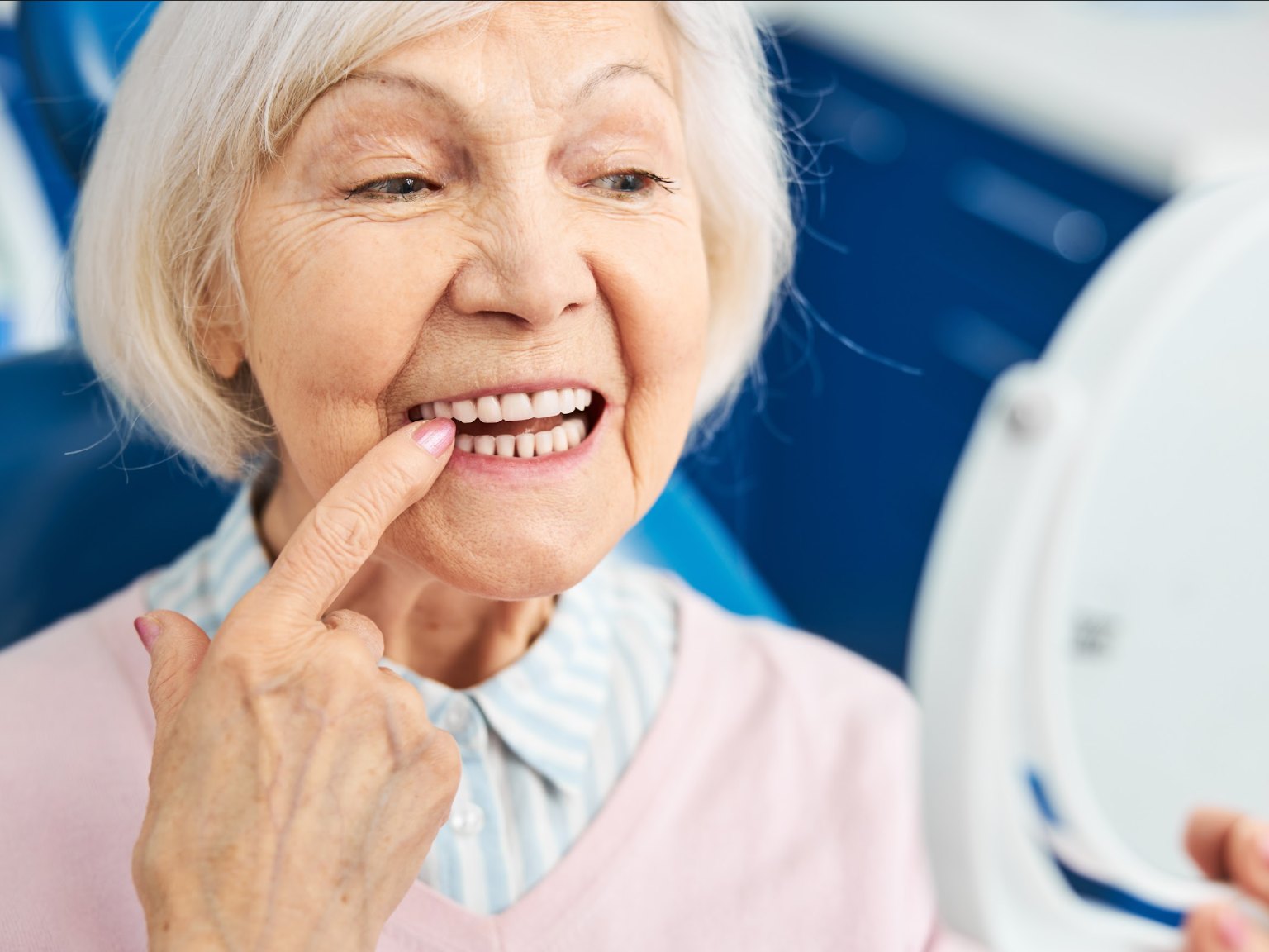 An older woman smiling and checking her teeth in a hand mirror