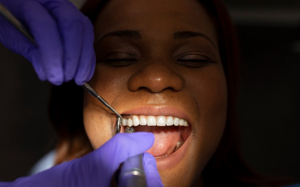 A relaxed patient smiling with her eyes closed while gloved hands examine her teeth
