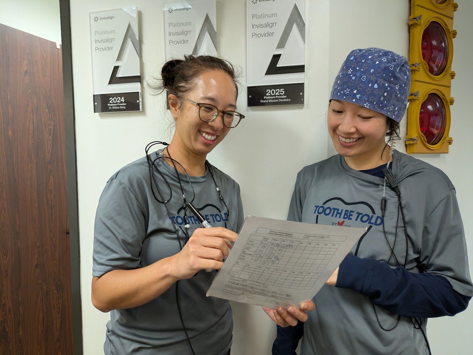 Two hygienists reading a chart under the practice's award plaques